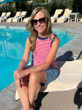 Woman sitting by a pool wearing a red and white striped tank top and denim shorts.