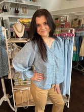 Woman wearing a light blue blouse and beige pants in a clothing store.