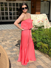 Woman in a coral strapless dress standing outdoors on a patio.