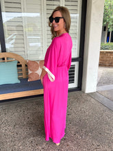 Woman in a bright pink dress standing outside a house.