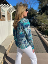 Woman wearing a blue and teal patterned blouse and sunglasses outdoors.