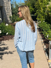 Woman in a striped shirt and jeans walking outdoors on a sunny day.