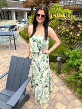 Woman in a green and white patterned dress standing outdoors in a garden setting.