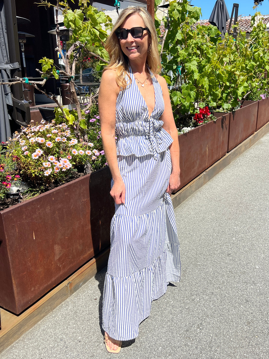 Navy blue and white pinstripe set with the top featuring a halter style, ties in the front and a low cut neckline. The maxi skirt features an elastic waist with tiered sections and a side slit.