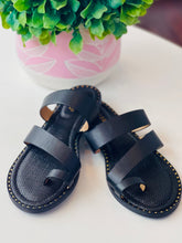 Pair of black sandals on a white surface with a potted plant in the background