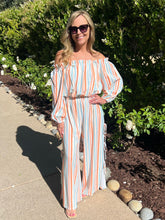 Woman in a striped off-shoulder outfit standing outdoors with greenery in the background