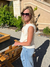 Woman standing outdoors near a wooden bench with a building and greenery in the background