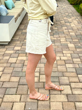Person wearing a light-colored top and white shorts on a paved outdoor area.