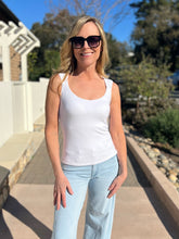 Woman wearing a white sleeveless top and light blue jeans standing outdoors.