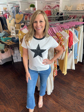 Woman wearing a white t-shirt with a black star in the center, standing in front of a clothing rack.