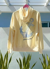 Yellow hoodie with an anchor design hanging on a rack outdoors.