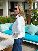 Woman in a white jacket and sunglasses standing in front of a blue outdoor sofa.