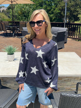 Woman wearing a navy sweater with white star patterns outdoors on a patio.
