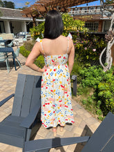 Woman in a colorful dress standing outdoors near a patio area with chairs and plants.