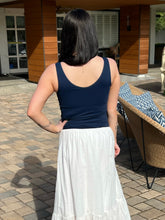 Woman wearing a navy tank top and white skirt standing outdoors on a patio.