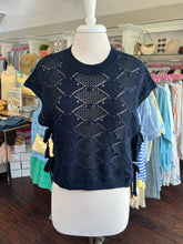 Navy blue knitted short sleeve sweater on a mannequin in a store setting with clothing racks in the background.