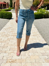 Person wearing light blue jeans standing on a stone pathway with greenery in the background