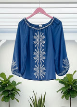 Blue blouse with white embroidery on a pink hanger against a white background