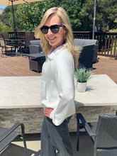 Woman in a white blouse and sunglasses standing outdoors on a patio.