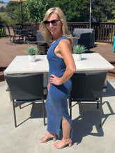 Woman in a blue dress standing outdoors near a table with chairs.