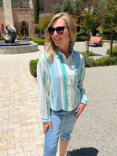 Woman wearing a striped shirt and sunglasses outdoors with a building and fountain in the background