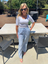 Woman standing outdoors on a patio with outdoor furniture and greenery.