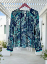 Blue and teal patterned blouse on a hanger with a blurred background