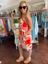 Woman in a colorful dress standing in a clothing store with racks of clothes in the background.