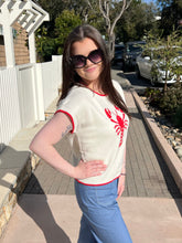 Woman wearing a cream sweater with a red lobster design outdoors.