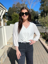 Woman wearing sunglasses and a white blouse with black pinstripe pants outdoors.