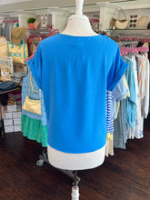 Bright colbalt blue top showing back view on a mannequin in a store setting with various items in the background