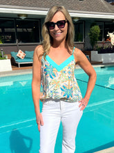 Woman in a floral top and white pants standing by a pool
