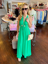 Woman standing in a store wearing a green halter maxi dress.