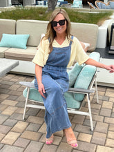 Woman in denim overalls sitting on a patio chair with outdoor furniture in the background