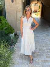 Woman in a white dress standing on a stone path with plants and a building in the background