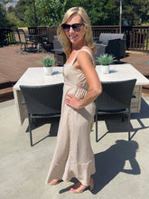Woman in a beige dress standing on a patio with outdoor furniture and plants.