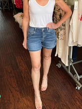 Person wearing a white tank top and blue denim shorts in a store setting.