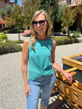 Woman in a teal top and jeans standing outdoors with trees and a building in the background