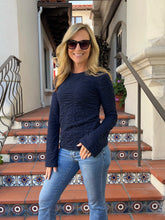 A woman wearing a dark navy blue long-sleeve textured knit top and light blue jeans, standing on tiled outdoor stairs.