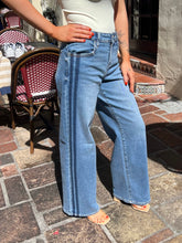 A person wearing light blue wide-leg denim jeans with double vertical seams, standing on a stone patio.