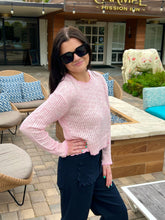 Woman in pink sweater and sunglasses standing outdoors near a building with 'Carmel Mission Inn' sign.