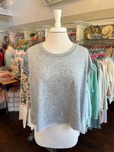Gray tank top on a mannequin in a store setting with racks of clothes in the background.