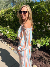 Woman in a striped top and pants standing outdoors with greenery in the background