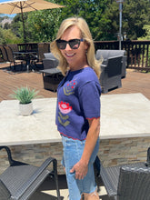 Woman wearing sunglasses and a blue floral sweater standing outdoors on a patio.