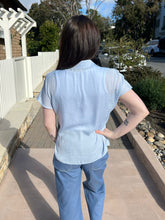Woman wearing a halogen blue top and pants standing outdoors on a sidewalk.