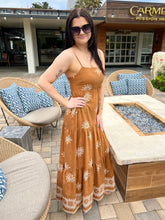 Woman in a brown dress standing in front of a building with outdoor seating area.