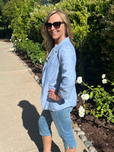 Woman in a blue jacket and jeans standing outdoors near a garden path.