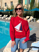 Woman wearing a red sweater with a sailboat design by a poolside.