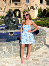 Woman in a blue dress standing in front of a fountain and building
