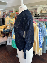 Navy blue knitted short sleeve sweater side view on a mannequin in a store setting with clothing racks in the background.